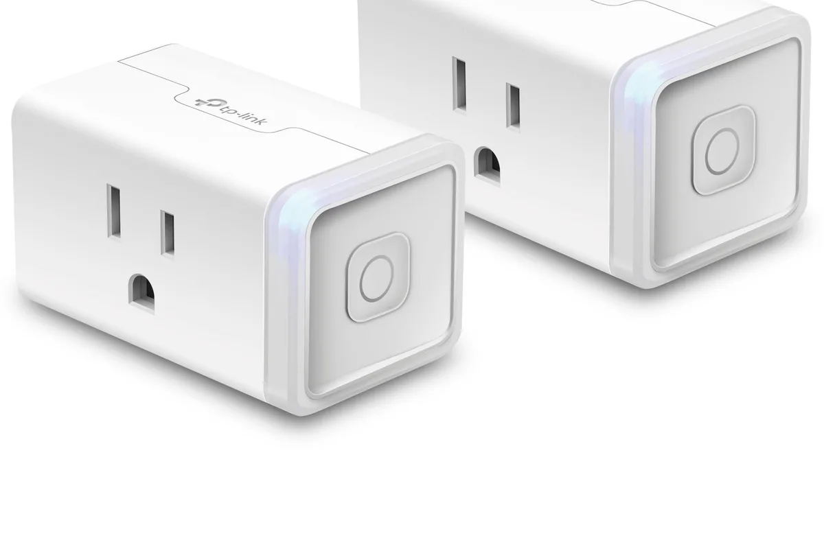 A compact smart plug plugged into a wall outlet beside a lamp